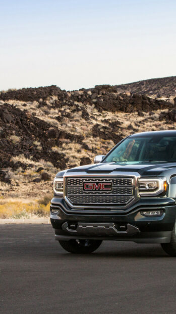 A dark GMC truck is parked near a rugged rocky terrain under a clear sky showing GMC Wallpapers, HD Phone Wallpaper