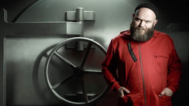 A man wearing a red suit stands confidently near a large vault door in the Money Heist series, 4K Desktop Wallpaper