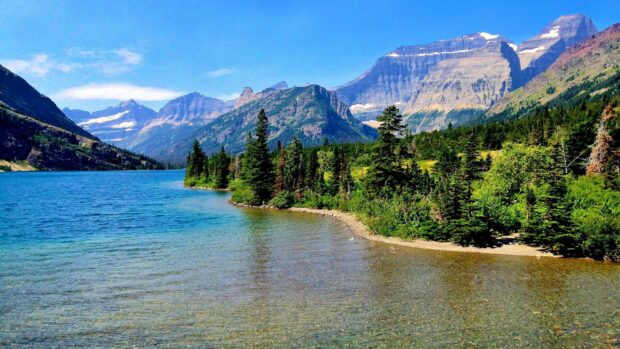 A clear lake surrounded by green trees and towering mountains in Montana, 2K Desktop Wallpaper