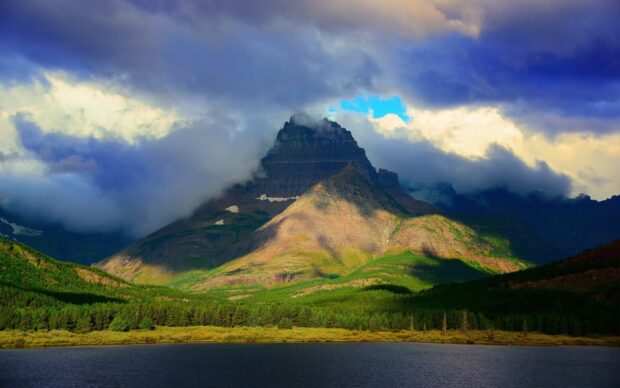 A mountain in Montana is partially covered by clouds above a forest and lake, HD Desktop Wallpaper