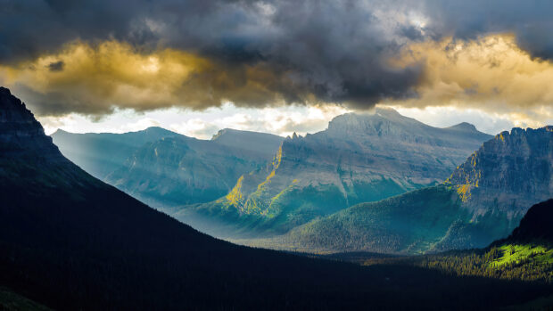 A vast Montana mountain range is illuminated by sunlight breaking through heavy clouds, Desktop Wallpaper