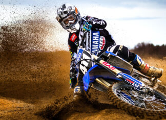 A motocross rider kicks up dirt while turning on the muddy track, 4K Desktop Wallpaper