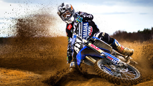 A motocross rider kicks up dirt while turning on the muddy track, 4K Desktop Wallpaper