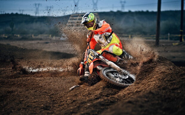 A motocross rider is speeding through muddy terrain kicking up dirt during a race, HD Desktop Wallpaper