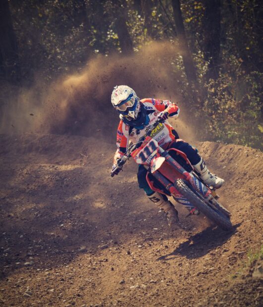 A motocross rider is turning sharply while kicking up dirt on a forest trail, HD Mobile Wallpaper