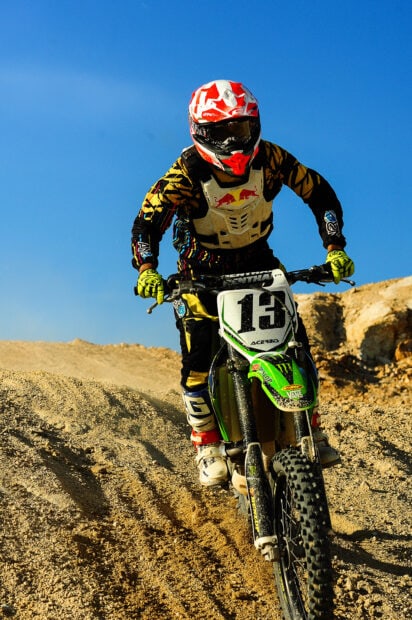 A motocross rider wearing protective gear is jumping on a dirt track under a clear blue sky, HD Mobile Wallpaper