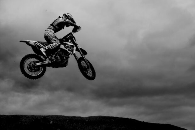 A motocross rider is captured mid air during a jump over a dirt hill under a cloudy sky, 2K Desktop Wallpaper