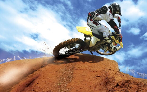 A motocross rider in full gear rides over a dirt jump with a clear blue sky, HD Desktop Wallpaper