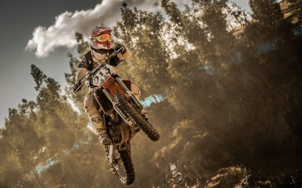 A motocross rider in full gear jumping over a dusty track during a race, HD Desktop Wallpaper