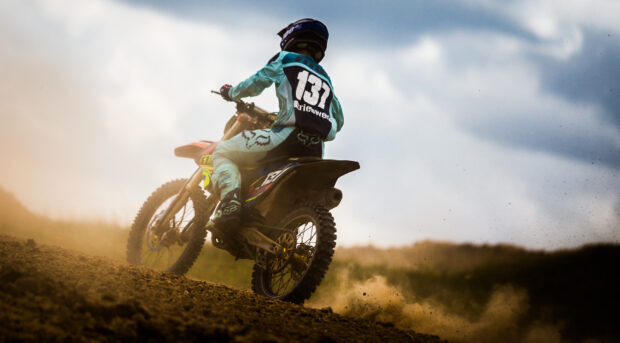 A motocross rider races through a dirt track under a cloudy sky, HD Desktop Wallpaper