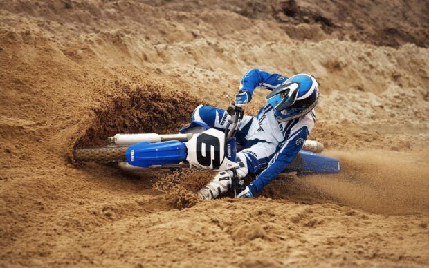 A motocross rider wearing blue gear is racing on a dirt track kicking up sand and dust, HD Desktop Wallpaper