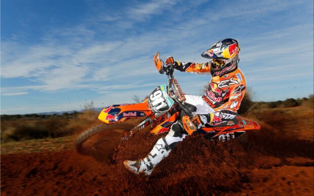 A motocross rider is sharply turning with dirt flying on a sunny day, 2K Desktop Wallpaper