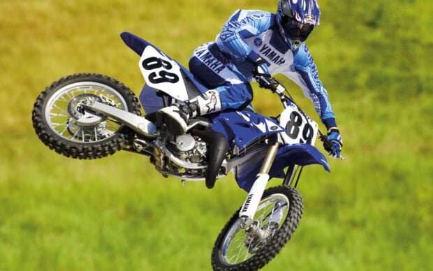 A motocross rider in full gear is jumping on a blue Yamaha bike in an outdoor field, HD Desktop Wallpaper