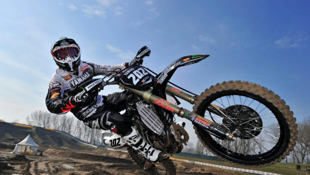 A motocross rider is performing an impressive jump on a dirt track during a race, 4K Desktop Wallpaper