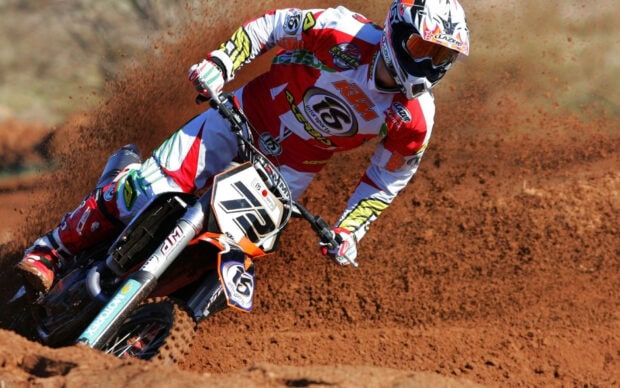 A motocross rider wearing protective gear races on a dirt track kicking up mud, HD Desktop Wallpaper