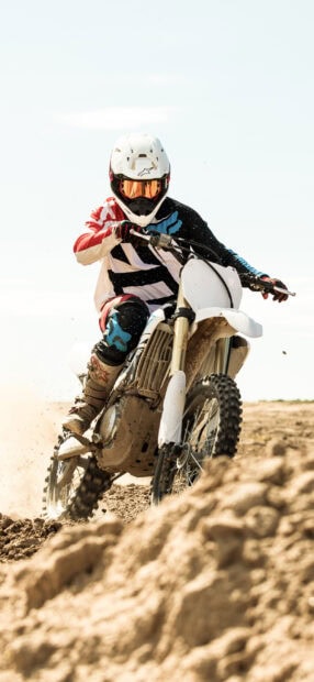 A motocross rider is speeding through a dusty dirt track on a white bike in intense action, 2K Phone Wallpaper