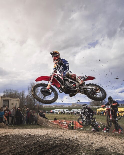 A motocross rider is jumping high over the dirt track during a race with spectators watching, 2K Mobile Wallpaper