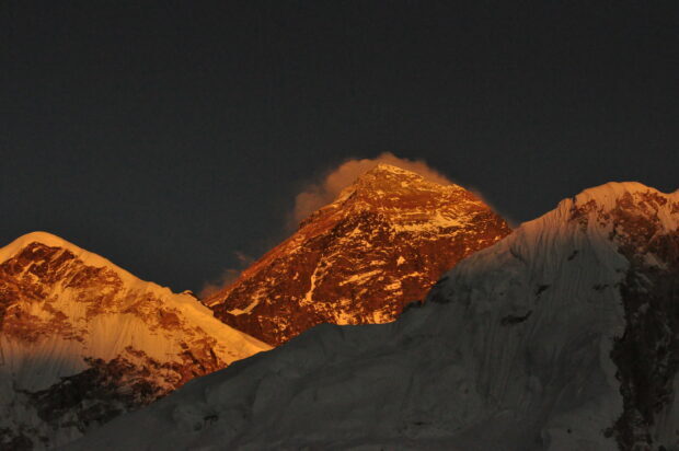 Mount Everest glows orange at sunset showing the peak's rugged features