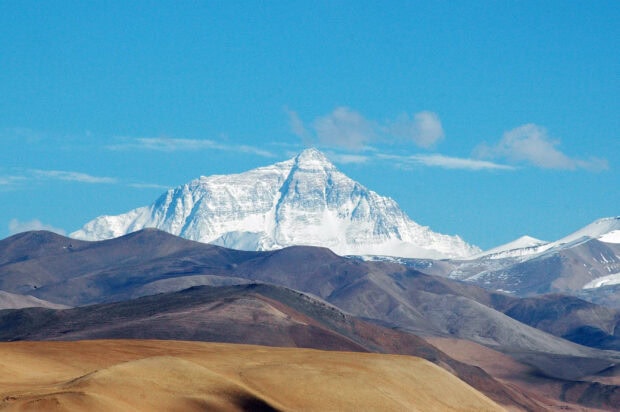 Snow covered Mount Everest standing tall amidst brown mountain ranges under clear blue sky
