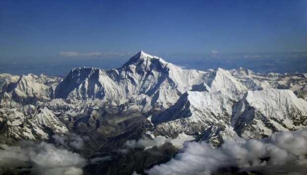 Snow covered Mount Everest dominates the mountain range under a clear blue sky