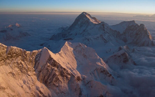 Snow covered Mount Everest stands tall above clouds during sunset with scenic mountain ridges visible