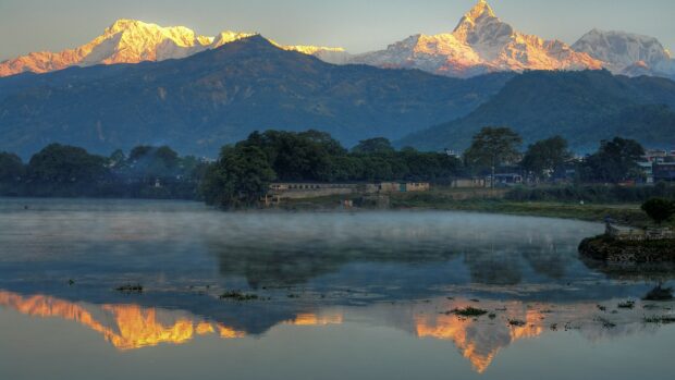 Mount Everest with sunlit peaks reflected in the calm river and mist over the water
