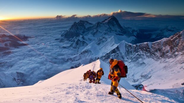 Climbers ascending Mount Everest amid snowy peaks and a sea of clouds at sunrise