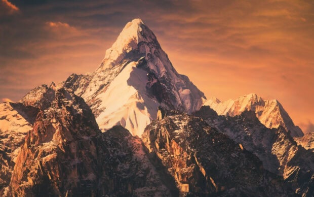 Snow covered Mount Everest peak glowing under a dramatic sunset sky