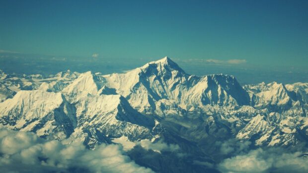 Snow covered Mount Everest towering above clouds in a clear sky view