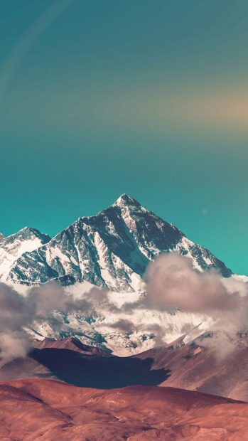 Snow capped Mount Everest peak surrounded by clouds and clear sky
