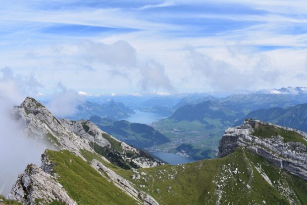 A scenic view of Mount Pilatus with green slopes and distant lakes under a cloudy sky