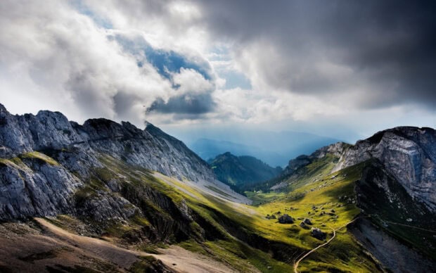 Rocky terrain and grassy slopes of Mount Pilatus under a cloudy sky with sun rays breaking through