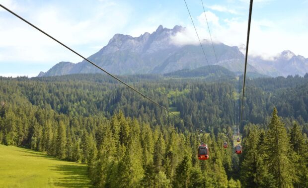 Cable cars traveling over green forest at Mount Pilatus in clear weather