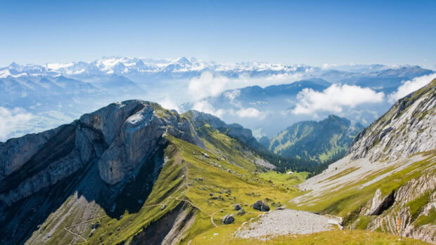 A breathtaking view of Mount Pilatus with green slopes and distant snowy peaks in clear weather