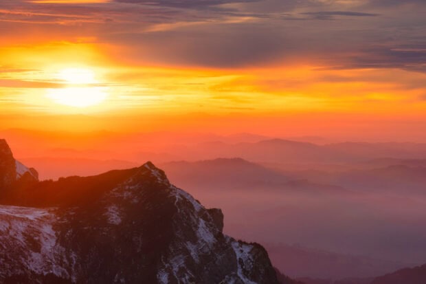 Mount Pilatus mountain with snow covered peaks under a vibrant orange sunset sky