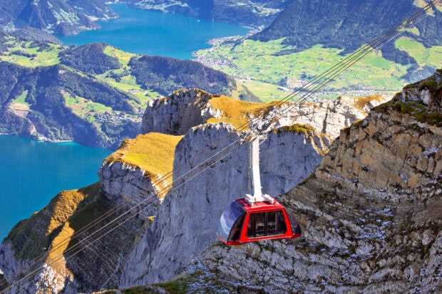 Red cable car climbing rocky Mount Pilatus with green valley and lake in the background