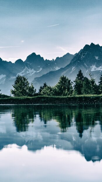 A serene mountain lake reflects the surrounding trees and peaks under a clear sky, 2K Phone Wallpaper