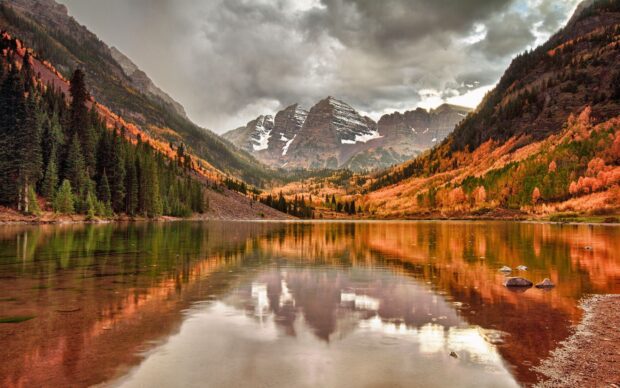 A mountain lake reflects the cloudy sky and autumn trees in a peaceful landscape, 2K Desktop Wallpaper