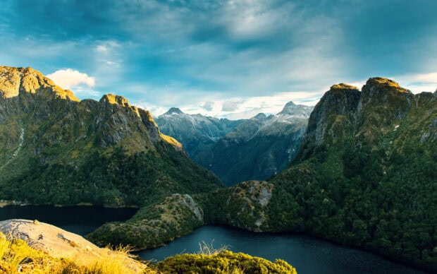 A mountain valley with lush greenery and a calm lake under a partly cloudy sky, 2K Desktop Wallpaper