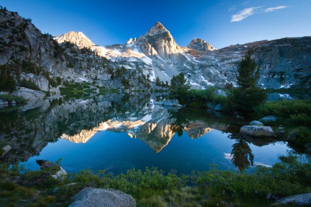 A clear mountain lake reflects rocky peaks under a blue sky in this mountain lake wallpapers scene, 2K Desktop Wallpaper