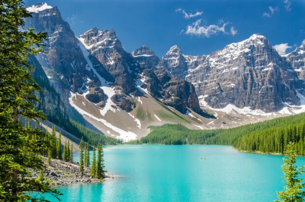 A turquoise mountain lake reflects snowy peaks and green forest under a clear blue sky, HD Desktop Wallpaper