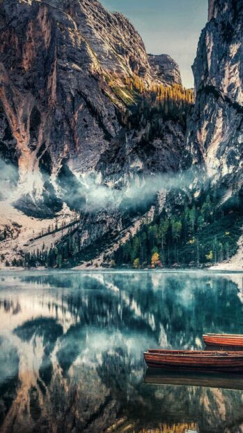 A serene mountain lake in Bulgaria reflects rocky cliffs and pine trees with two wooden boats floating calmly