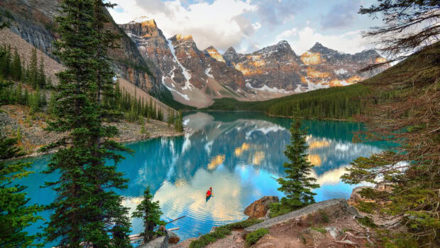 A red canoe floats on a calm mountain lake surrounded by pine trees and rocky cliffs, 4K Desktop Wallpaper