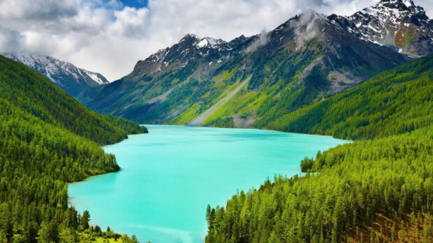 A clear turquoise mountain lake surrounded by dense green forests and snow capped peaks, 4K Desktop Wallpaper