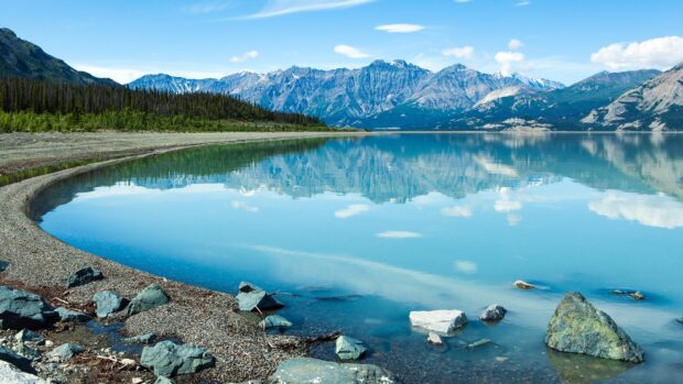 A clear mountain lake reflects surrounding rocky peaks and green forest, 4K Desktop Wallpaper