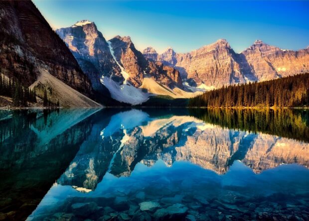 A clear mountain lake reflects towering rocky peaks under a bright blue sky, 2K Desktop Wallpaper
