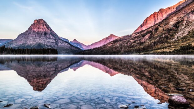 A clear lake reflects the rugged mountain peaks at Glacier National Park, 4K Desktop Wallpaper