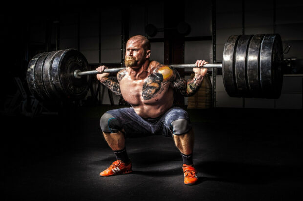 A muscular man with tattoos lifts a heavy barbell during powerlifting training in a gym, 2K Desktop Wallpaper