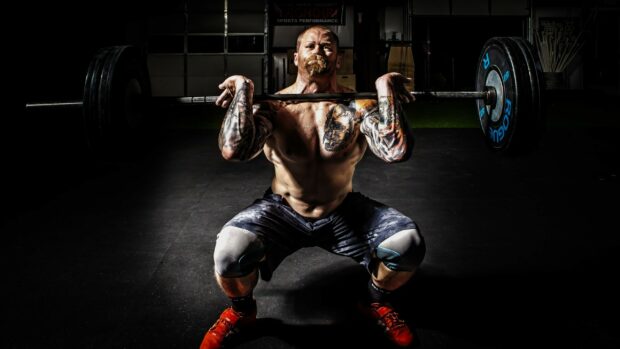 A muscular man is performing a clean and jerk in a gym with powerlifting wallpapers, 2K Desktop Wallpaper