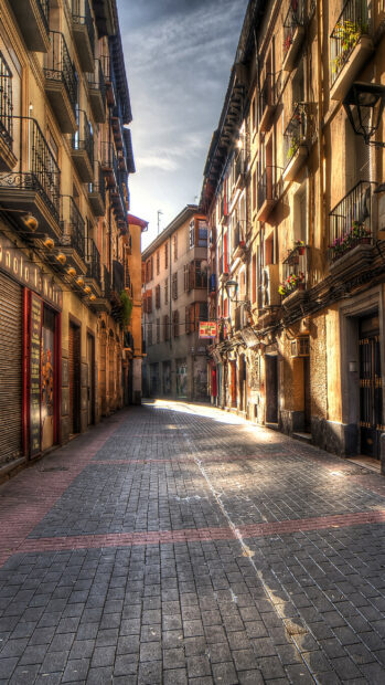 A narrow cobblestone street with historic buildings illuminated by sunlight in Spain, 2K Mobile Wallpaper